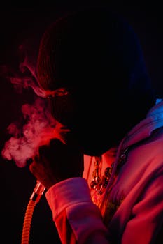 Silhouette of a person smoking in a balaclava, illuminated by red light.