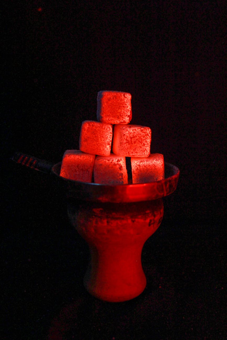 Glowing red hookah coals stacked on a traditional holder against a black background.